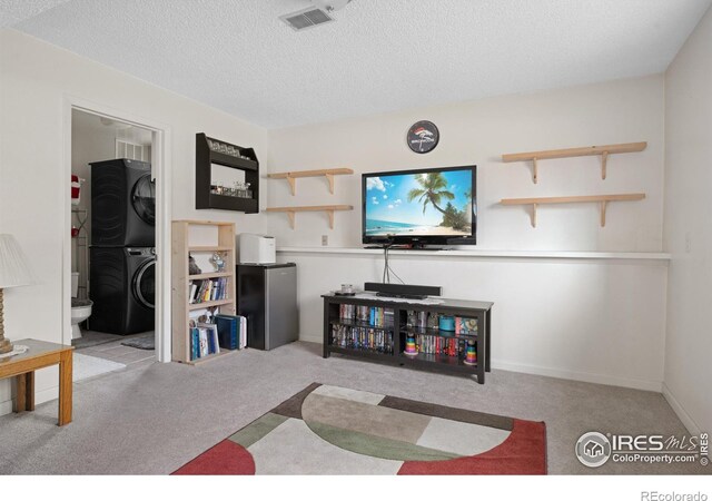 carpeted living room featuring visible vents, a textured ceiling, stacked washer / drying machine, and baseboards