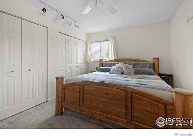 bedroom with carpet floors, a textured ceiling, ceiling fan, and multiple closets