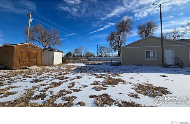 yard covered in snow with an outbuilding, a storage shed, and fence