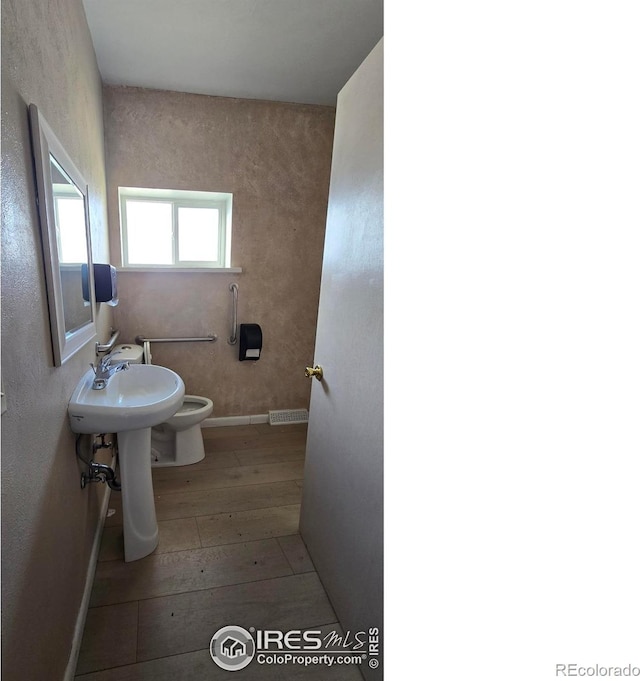 bathroom featuring visible vents, toilet, a sink, hardwood / wood-style floors, and baseboards