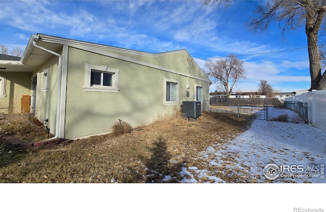 view of home's exterior featuring stucco siding, central AC, and fence