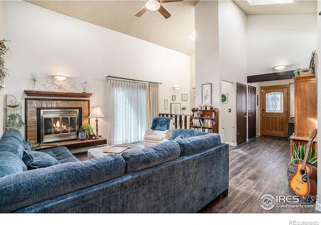 living room with ceiling fan, dark wood finished floors, a skylight, a glass covered fireplace, and high vaulted ceiling