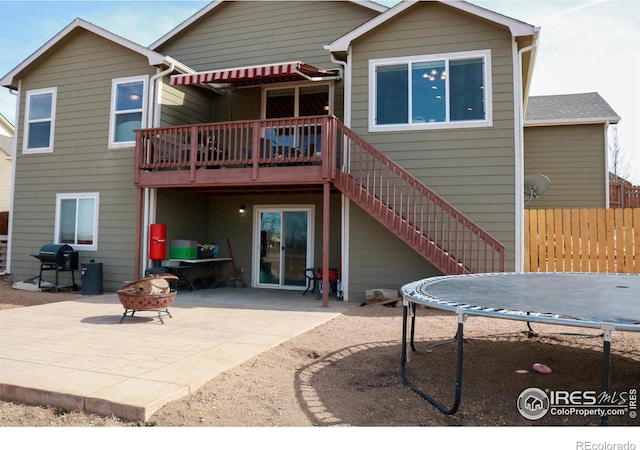 rear view of house with a patio, a trampoline, fence, an outdoor fire pit, and stairs