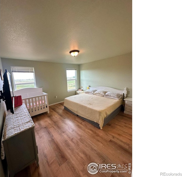 bedroom with wood finished floors, baseboards, and a textured ceiling