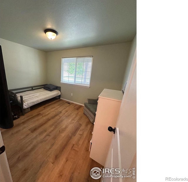 bedroom with wood finished floors, baseboards, and a textured ceiling