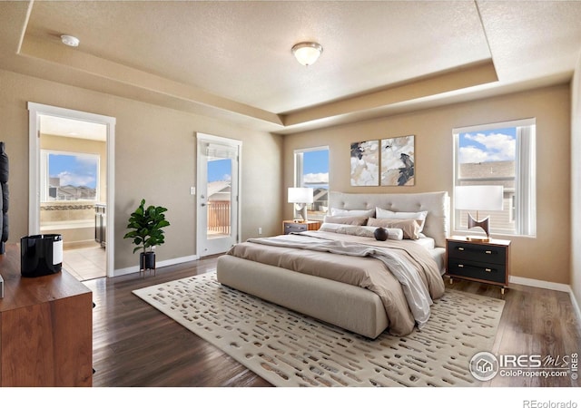 bedroom featuring access to exterior, a raised ceiling, wood finished floors, and baseboards