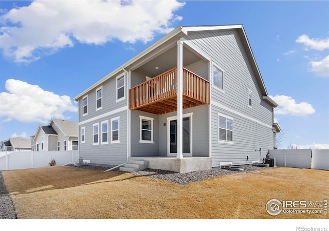 rear view of house featuring a balcony and a fenced backyard