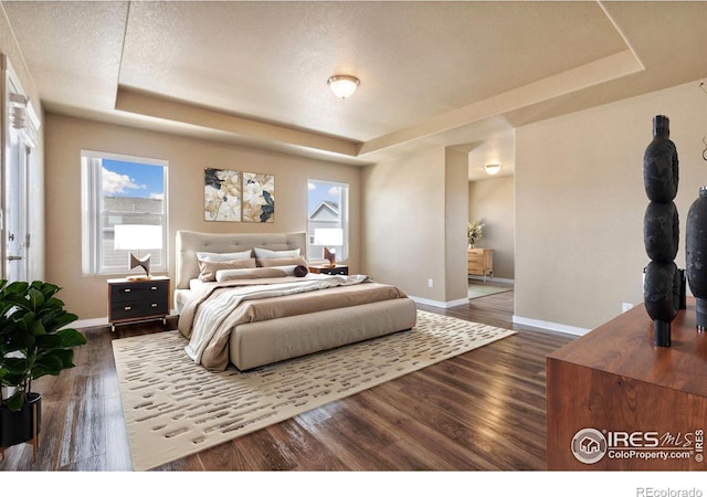 bedroom featuring baseboards, a raised ceiling, and dark wood-type flooring