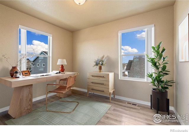 home office with plenty of natural light, wood finished floors, visible vents, and baseboards