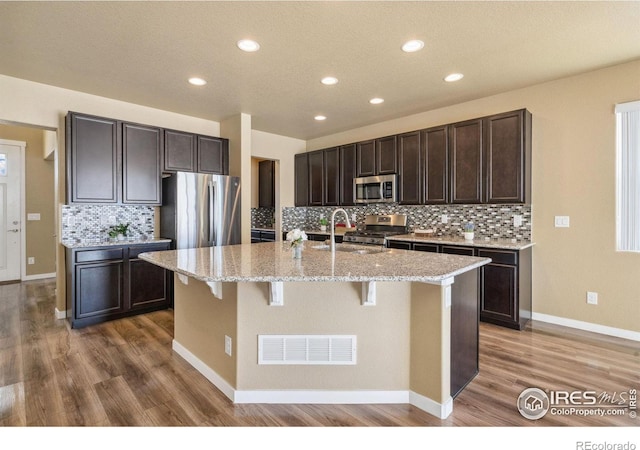 kitchen with visible vents, dark brown cabinets, an island with sink, stainless steel appliances, and a sink