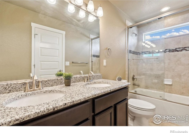 bathroom featuring double vanity, shower / bath combination with glass door, toilet, and a sink