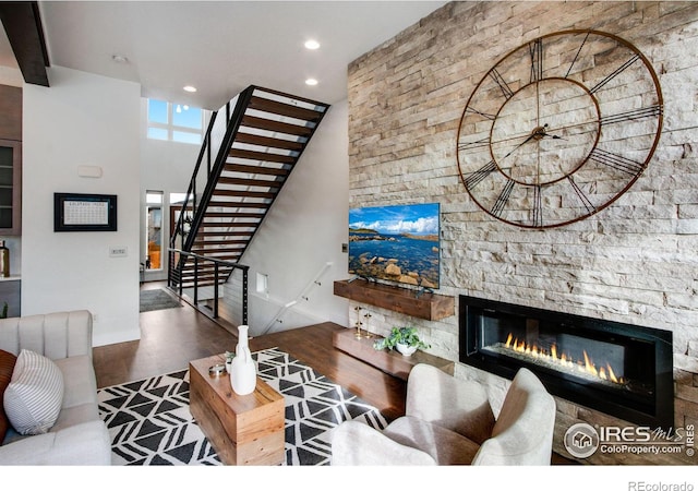 living room with stairway, wood finished floors, recessed lighting, a stone fireplace, and a towering ceiling