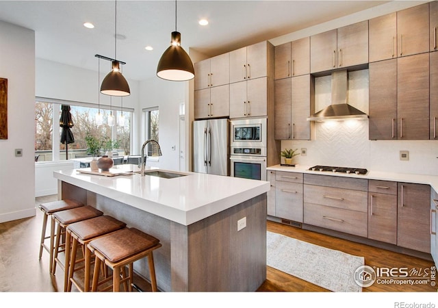 kitchen featuring a sink, stainless steel appliances, wall chimney exhaust hood, decorative backsplash, and dark wood-style flooring