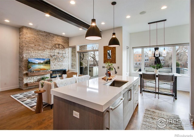 kitchen with pendant lighting, a kitchen island with sink, a sink, wood finished floors, and a fireplace