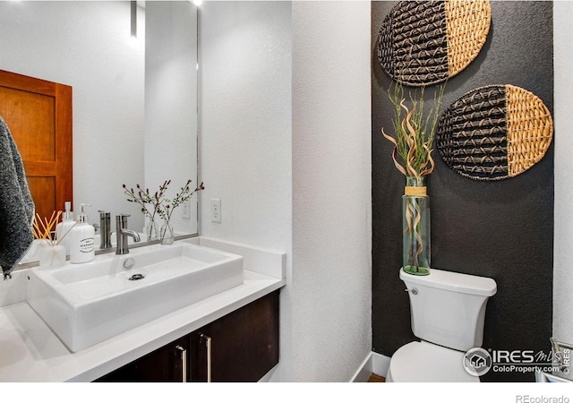 bathroom with toilet, vanity, and a textured wall