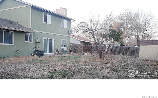 rear view of house with central AC unit, a chimney, and fence