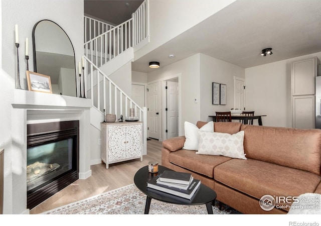 living area featuring a glass covered fireplace, stairs, and light wood-type flooring