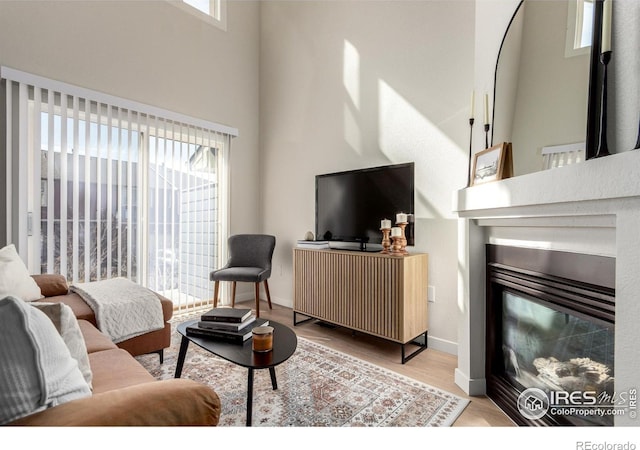 living room featuring a glass covered fireplace, a high ceiling, baseboards, and wood finished floors