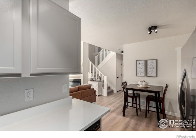 dining area with stairway, light wood-style floors, baseboards, and a textured ceiling