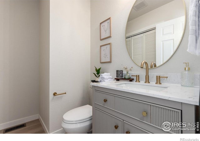 half bath featuring vanity, toilet, baseboards, and visible vents