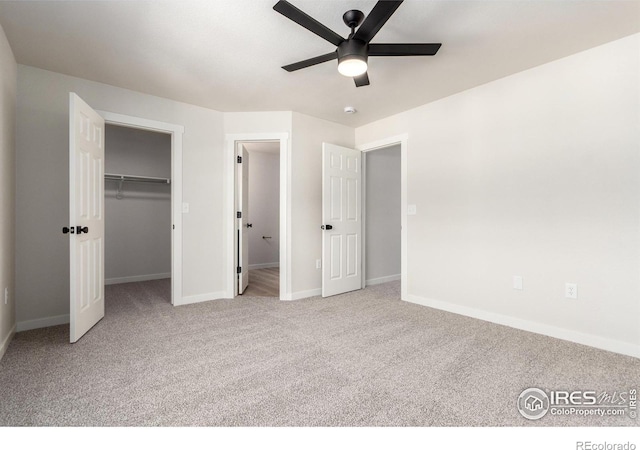 unfurnished bedroom with carpet flooring, a ceiling fan, a walk in closet, and baseboards