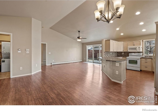 kitchen with a wealth of natural light, stacked washer and dryer, a baseboard heating unit, dark countertops, and white appliances