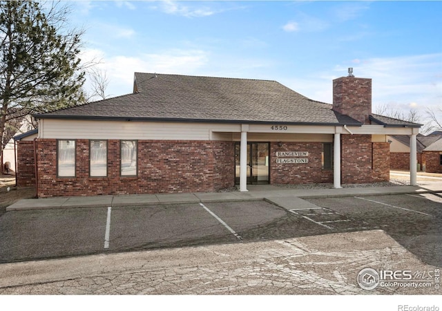 back of house featuring brick siding, a chimney, and a shingled roof