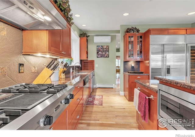 kitchen with built in appliances, light wood-style floors, baseboard heating, a sink, and exhaust hood