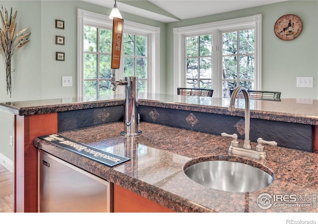 kitchen featuring a sink, dark stone counters, dishwashing machine, and decorative light fixtures