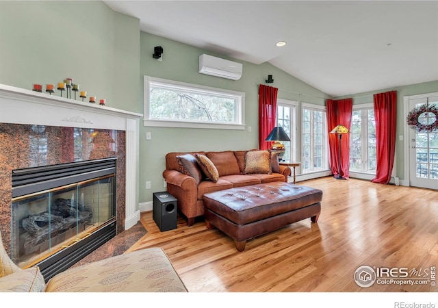 living area with wood finished floors, lofted ceiling, a wall mounted AC, and a healthy amount of sunlight