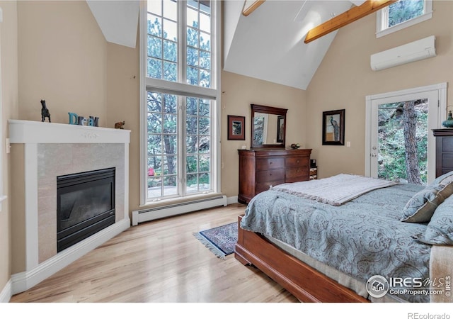bedroom featuring a wall mounted air conditioner, high vaulted ceiling, a glass covered fireplace, wood finished floors, and a baseboard radiator