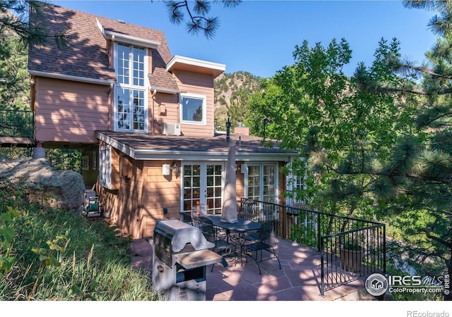 back of property with a shingled roof, french doors, and outdoor dining space