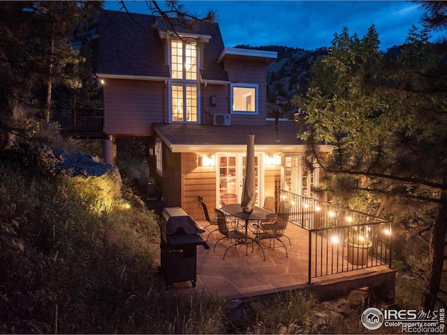back of house at twilight with a patio, roof with shingles, and french doors