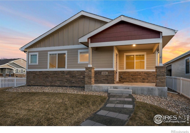 craftsman-style home featuring stone siding, board and batten siding, a front yard, and fence