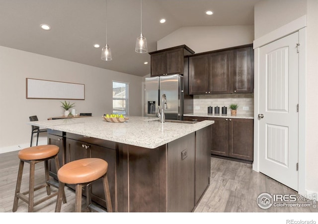 kitchen with dark brown cabinetry, a breakfast bar area, vaulted ceiling, stainless steel refrigerator with ice dispenser, and a sink