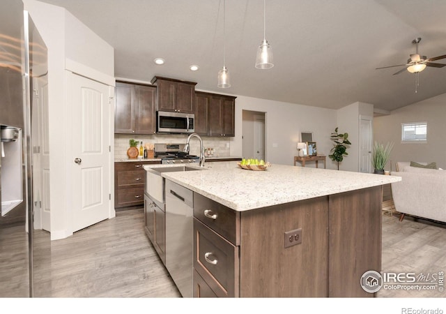 kitchen featuring open floor plan, stainless steel appliances, light wood-style floors, dark brown cabinetry, and decorative backsplash