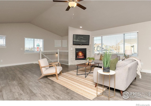 living room featuring lofted ceiling, wood finished floors, baseboards, a brick fireplace, and ceiling fan