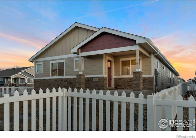 craftsman-style home with board and batten siding, stone siding, and a fenced front yard