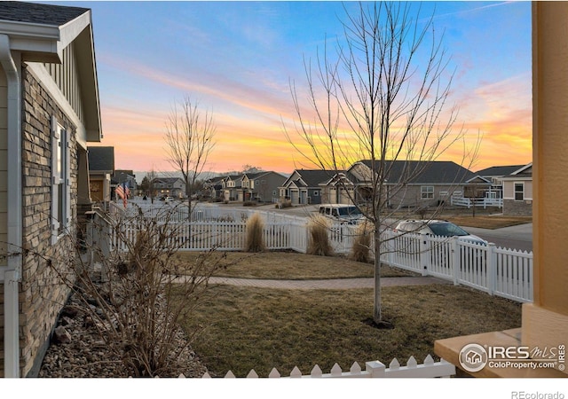 yard at dusk featuring fence and a residential view