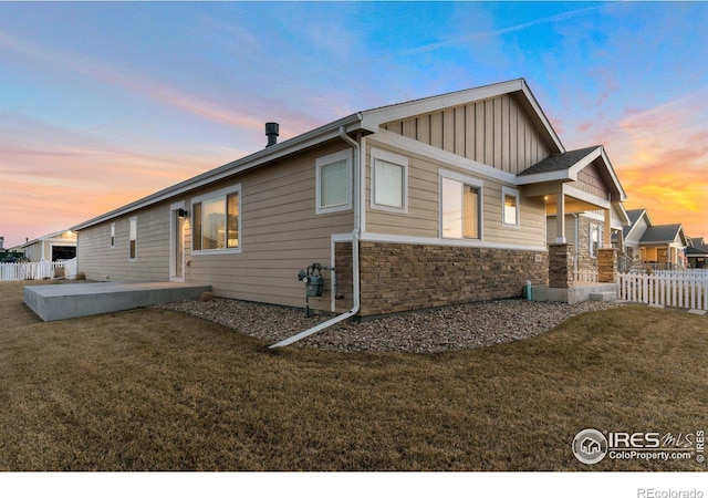 view of home's exterior with fence, a yard, stone siding, a patio area, and board and batten siding