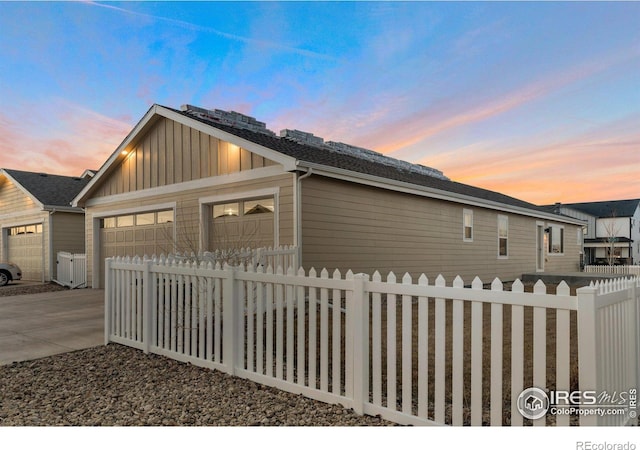 property exterior at dusk featuring a fenced front yard, a garage, and board and batten siding