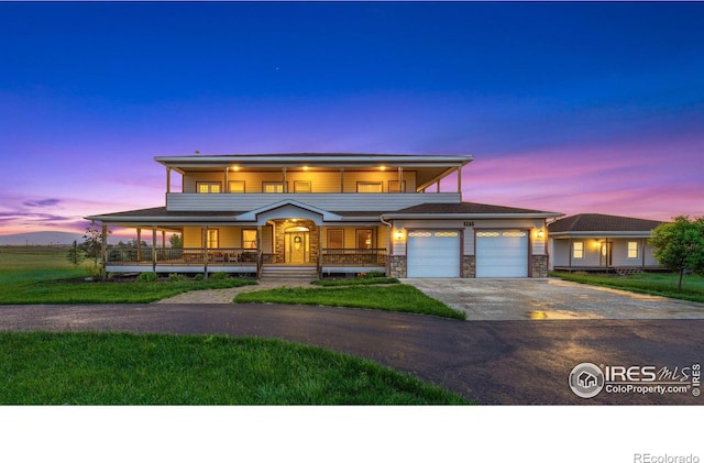 prairie-style house with a balcony, covered porch, concrete driveway, a front lawn, and stone siding