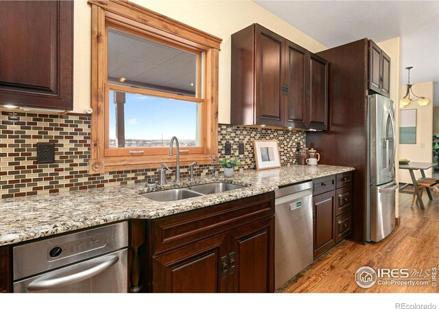 kitchen with a sink, dark brown cabinets, light wood-style floors, appliances with stainless steel finishes, and tasteful backsplash