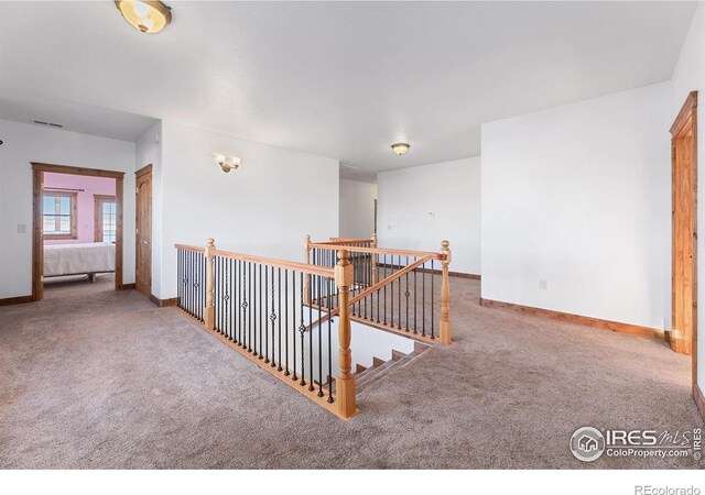 corridor with an upstairs landing, visible vents, baseboards, and carpet