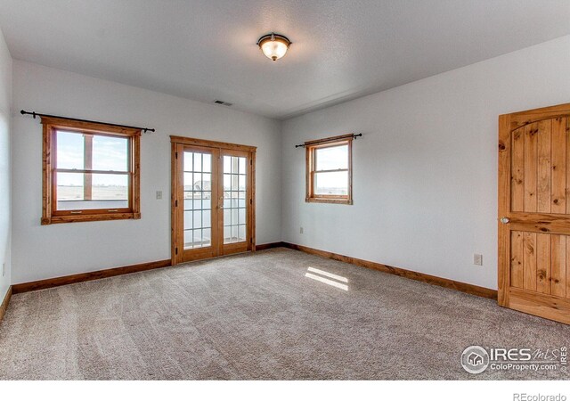 carpeted empty room with french doors, visible vents, and baseboards