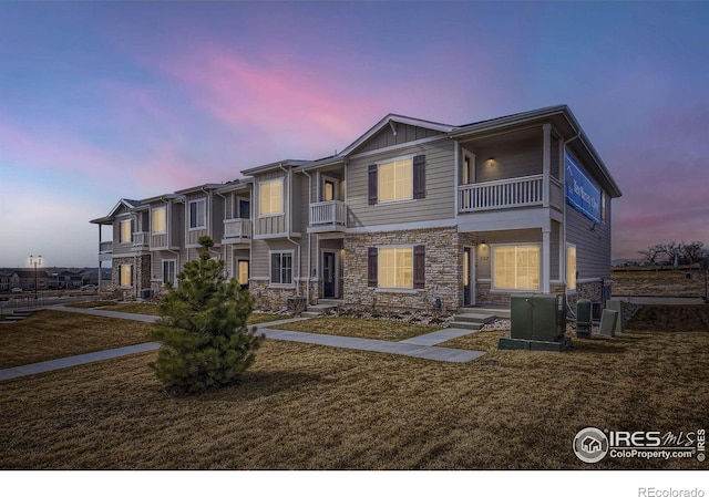 view of front of property with a balcony, a lawn, and stone siding