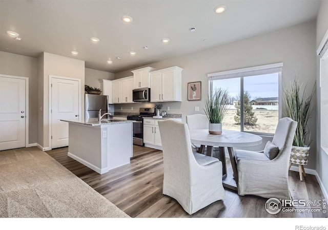 kitchen featuring wood finished floors, a center island with sink, recessed lighting, stainless steel appliances, and white cabinetry