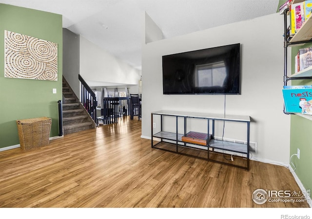 living area with vaulted ceiling, stairway, baseboards, and wood finished floors