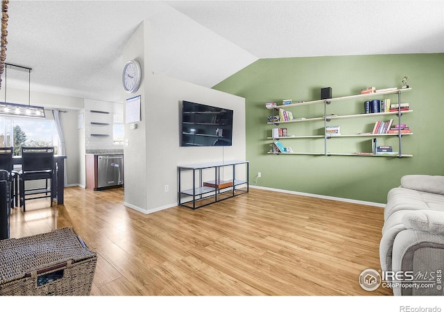 living area with vaulted ceiling, wood finished floors, baseboards, and a textured ceiling