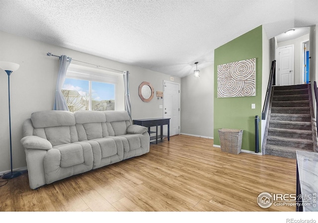 living area featuring a textured ceiling, wood finished floors, stairway, baseboards, and lofted ceiling